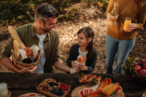 mutter, vater und tochter halten ihr essen beim picknick im wald - child vegetable squash corn stock-fotos und bilder