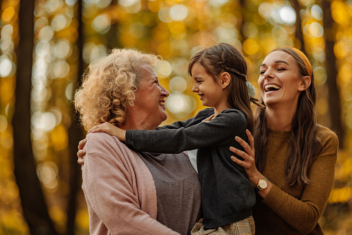 Grandmother, daughter and granddaughter are hugging while posing and smiling in the forest