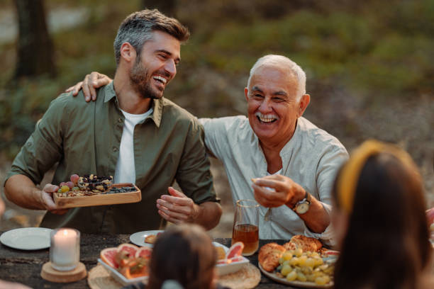 Father and grandfather having great time during a family picnic in forest Caucasian father and the grandfather are laughing and having a great time during family picnic in a forest during fall food recall stock pictures, royalty-free photos & images
