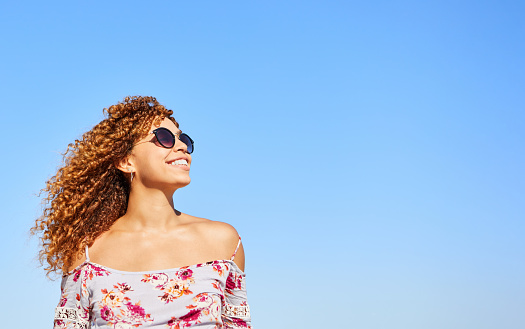 Young woman with braided hair and sunglasses smiling happily. Blue sky in the background