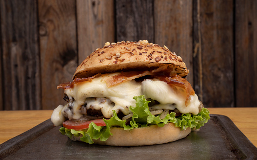 Giant burger. Closeup view of a delicious burger with danbo cheese, lettuce, tomato, onion, grilled meat, crispy bacon and potato with provolone bread, with a wooden background.