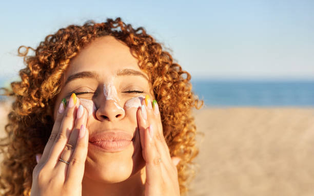 Smiling happy woman applying sunscreen to her face on the beach at sunset. Young latin woman applying sunscreen to her face on the beach in a summer sunset. Cheerful gesture with her eyes closed sunbathing stock pictures, royalty-free photos & images
