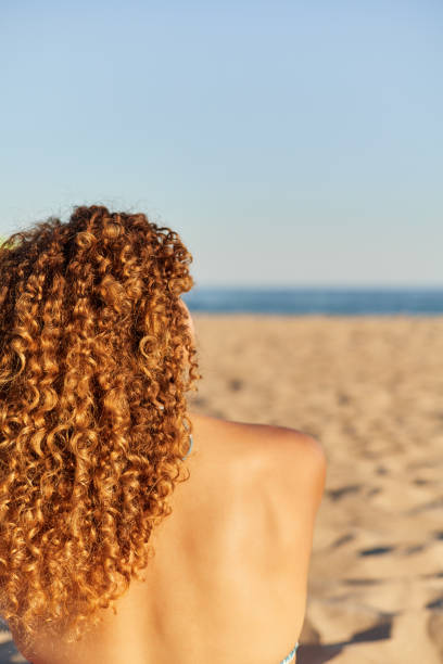 Woman sitting on the sand on the beach with the sea in the background. She is relaxing enjoying the sunset in summer