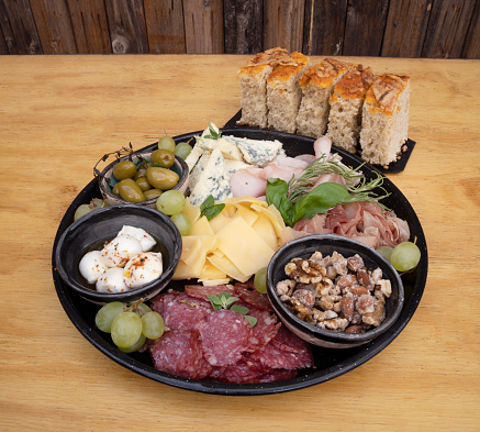 Antipasto. Closeup view of a dish with sliced salami, cheese, blue cheese, focaccia bread, italian boconccinos, walnuts, ham, cured ham and green olives on the wooden table.