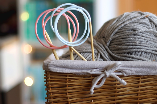 Basket with gray ball of yarn and knitting needles. Rainbow bookshelf in the background. Hygge at home. Selective focus.