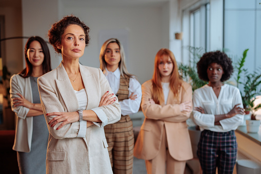 Serious businesswoman with serious face expression is standing in the corporate pose, posing in front of her female colleagues