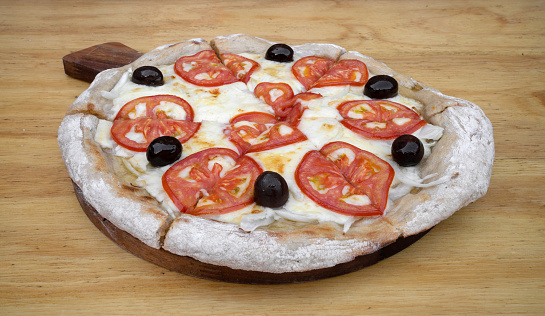 Closeup view of a traditional italian pizza with mozzarella cheese, tomato, garlic, onion and black olives, on the wooden table.