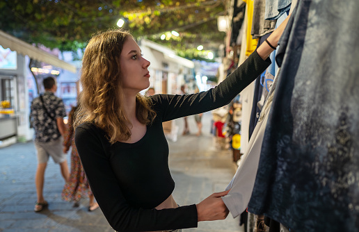 A girl chooses clothes for herself at a street market.