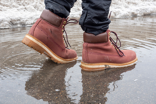 a man walks through a puddle in terracotta leather shoes. Close-up, reflection in a puddle, littered horizon. Walking man concept, journey, side view