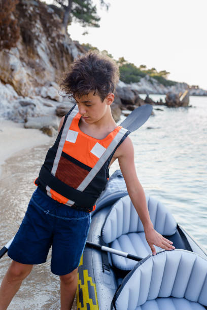 adolescente colocando seu colete salva-vidas pronto para explorar com caiaque inflável - summer camp child teenager kayak - fotografias e filmes do acervo