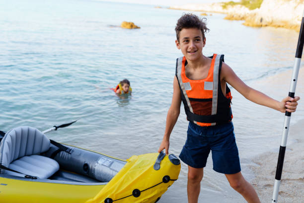 adolescente colocando seu colete salva-vidas pronto para explorar com caiaque inflável - summer camp child teenager kayak - fotografias e filmes do acervo