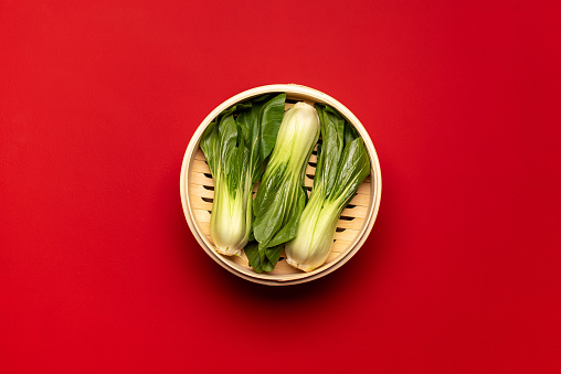 Top view with bok choy in a bamboo steamer isolated on a red background