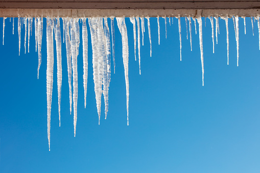 Close-up of shiny icicles on a roof gutter on a blue sky background. Space for copy.