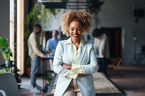 Professional African American businesswoman with a beaming smile, standing confidently in a contemporary office environment.