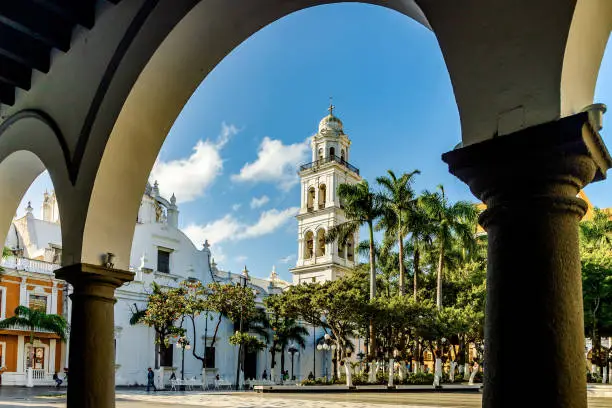 Bell tower of the Veracruz Cathedral known as Nuestra Señora de la Asunción, one of the symbolic buildings in the port, stands out for its white color that stands out among the palm trees of the Zócalo. The view is from the arcades of the Municipal Palace.