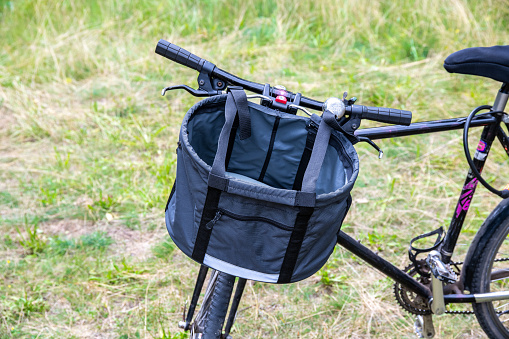 Detail of a bicycle's front basket mounted on the handlebar, set against a grassy background