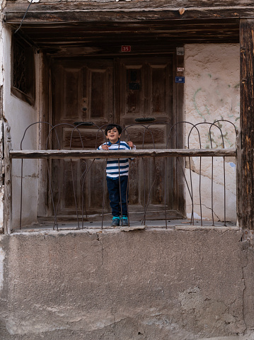 Little boy close the wooden door of their historical house and go out into the street. The entrance of the house is high. Stairs go down to the street from the right and left. Taken in daylight with a full frame camera.