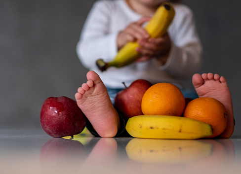 the baby is surrounded by fruit and is holding banana