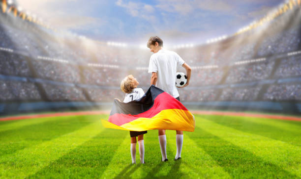 Germany football supporter on stadium. German fans on soccer pitch watching team play. Group of supporters with flag and national jersey cheering for Germany. Championship game.