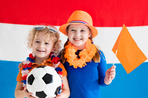 Children cheering and supporting Dutch football team. Kids fans and supporters of the Netherlands during soccer championship. Boy and girl from Holland with national flag and country symbols.