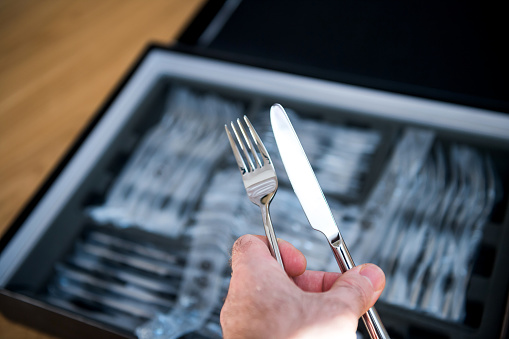 POV male hand holding new cutlery sets flatware with fork and knife being unboxed from the plastic package