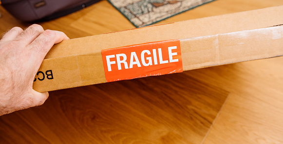 Fragile signage on the cardboard box of a new parcel delivered by freight transportation service pov male hand holding the box