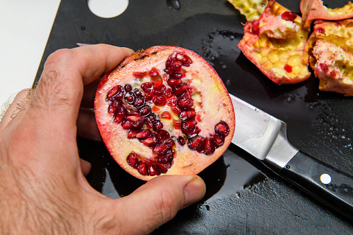Overhead view of male hand holding cut in half pomegranate with unique arrangements of red seeds inside - succulent bio organic fruit