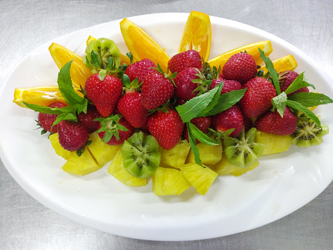 fresh and ripe fruits and berries on a large plate before serving. pineapple, kiwi, orange and strawberry are a delicious and healthy dessert for children and adults