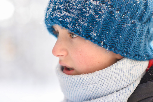 Portrait of a boy in a knitted hat and scarf in the snow