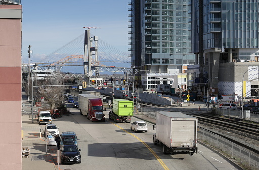 New Westminster, Canada - February 9, 2024: View from River Market walkway above Front Street by the railway tracks. Traffic crosses the level crossing on Begbie Street. New construction includes condo towers and the Pattullo Bridge replacement in the background.