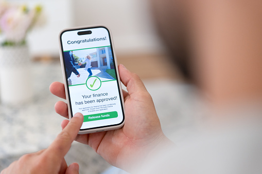 Man holding a digital with mortgage loan application approval. There is an image on the phone of a couple looking at their new house. Close up.