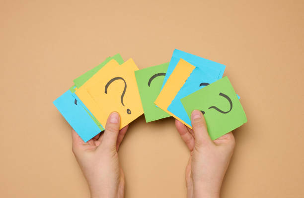 istock Female hands hold paper sheets with a drawn question mark on a beige background 2011348905