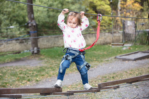 A little girl plays in an adventure park, balancing on some planks. She wears a protective sling.