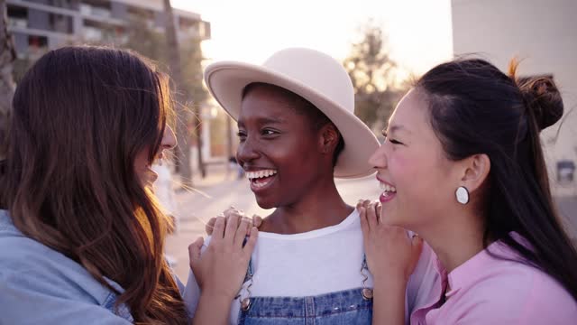 Joyful Caucasian and Asian friends join African girl who is posing outdoor looking camera laughing.