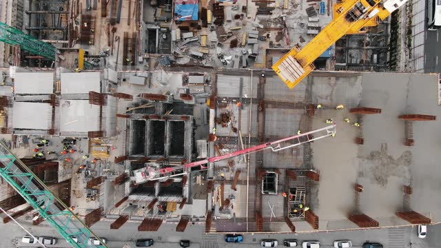 Flight over construction site between highways. Top down view of workers and construction cranes.