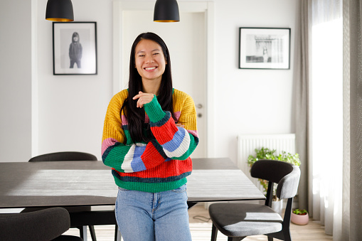 A happy Asian woman is posing in the living room leaning on the table.