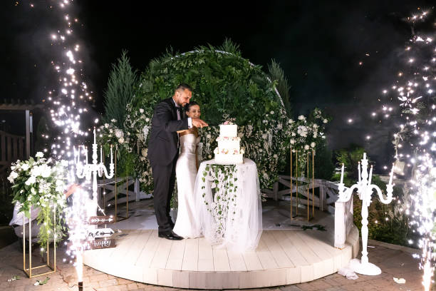 istock Bride and groom cutting stylish wedding cake at wedding reception in restaurant. Wedding couple holding knife and cutting together wedding cake decorated with flowers 2011487232