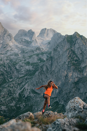 An extreme sportswoman is trail running and mountaineering and climbing the wild mountain. A female skyrunner is jumping on stones and rocks in mountains. A skyrunner is practicing for ultramarathon.