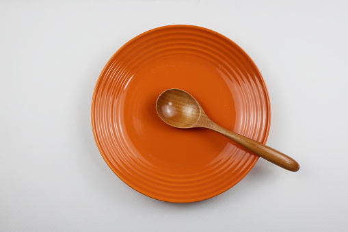 Orange plate and wooden spoon isolated on white background.