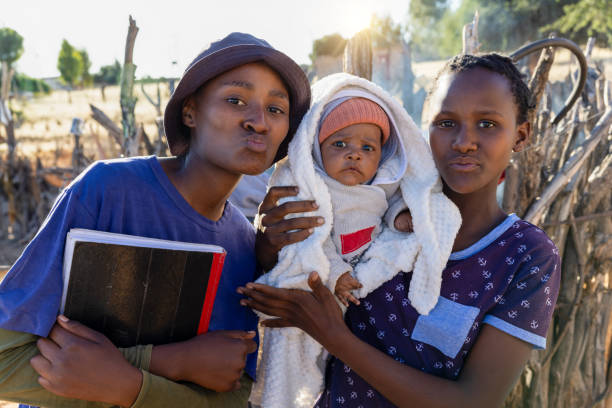 aldeia, adolescentes de escolas africanas com um bebê recém-nascido e livros escolares na mão - teenage pregnancy mother social issues family - fotografias e filmes do acervo