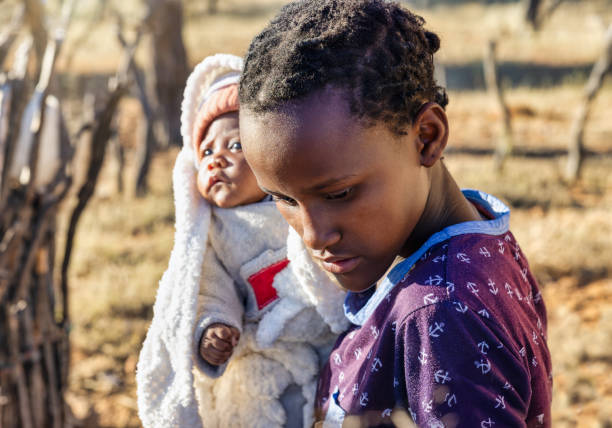 wioska, afrykański nastolatek i dziecko, stojący na podwórku - teenage pregnancy mother social issues family zdjęcia i obrazy z banku zdjęć