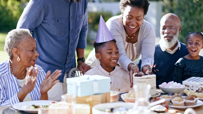 Happy family, child and cake in outdoor, birthday and celebration with grandparents, park and food. Singing, smile and happiness with presents, together and parent for childhood, applause and son