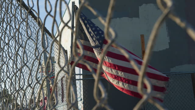 American flag, abandoned and fence with material, torn and tattered for memorial and veterans. Memorial day, damage and decay for injustice, remembrance and symbolism for inequality, rot and liberty