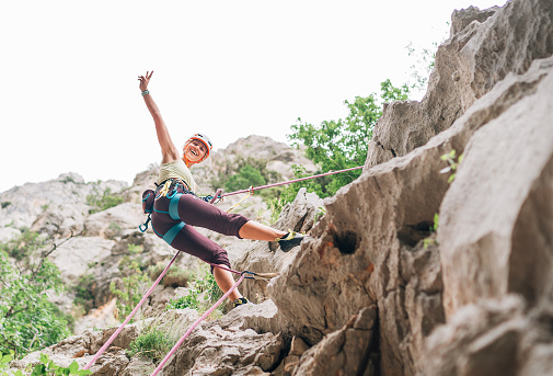 Smiling athletic woman in protective helmet and shoes climbing cliff rock wall using top rope and harness in Paklenica National park site in Croatia. Active extreme sports time spending concept