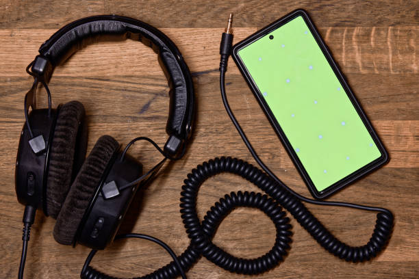istock Professional studio headphones with a coiled cable on a wooden surface, with phone had a green screen, full jack plug, top view 2011630563