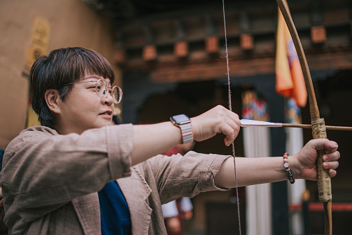 Asian Chinese female tourist practicing archery aiming and shooting in field