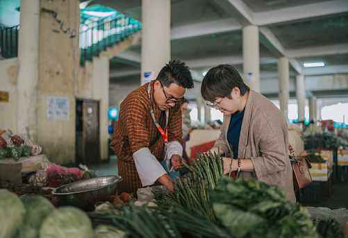 Bhutanese tour guide explaining showing to female tourist on local farmer's market