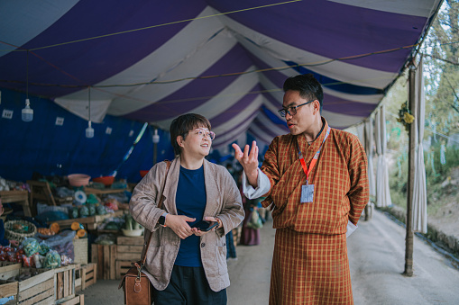Bhutanese tour guide explaining to female tourist on local farmer's market culture