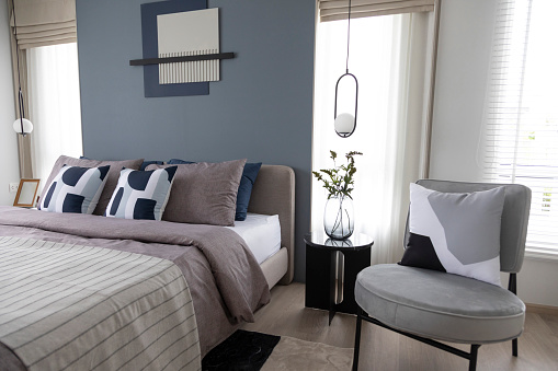 Stylish Bedroom with gray fabric headboard and bed with soft blue and white pillows setting. Cozy bedroom with art wall.