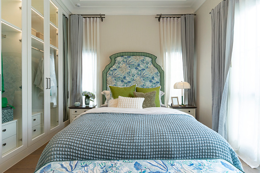 Interior view of luxury decorated green and blue headboard bedroom with side table lamp.